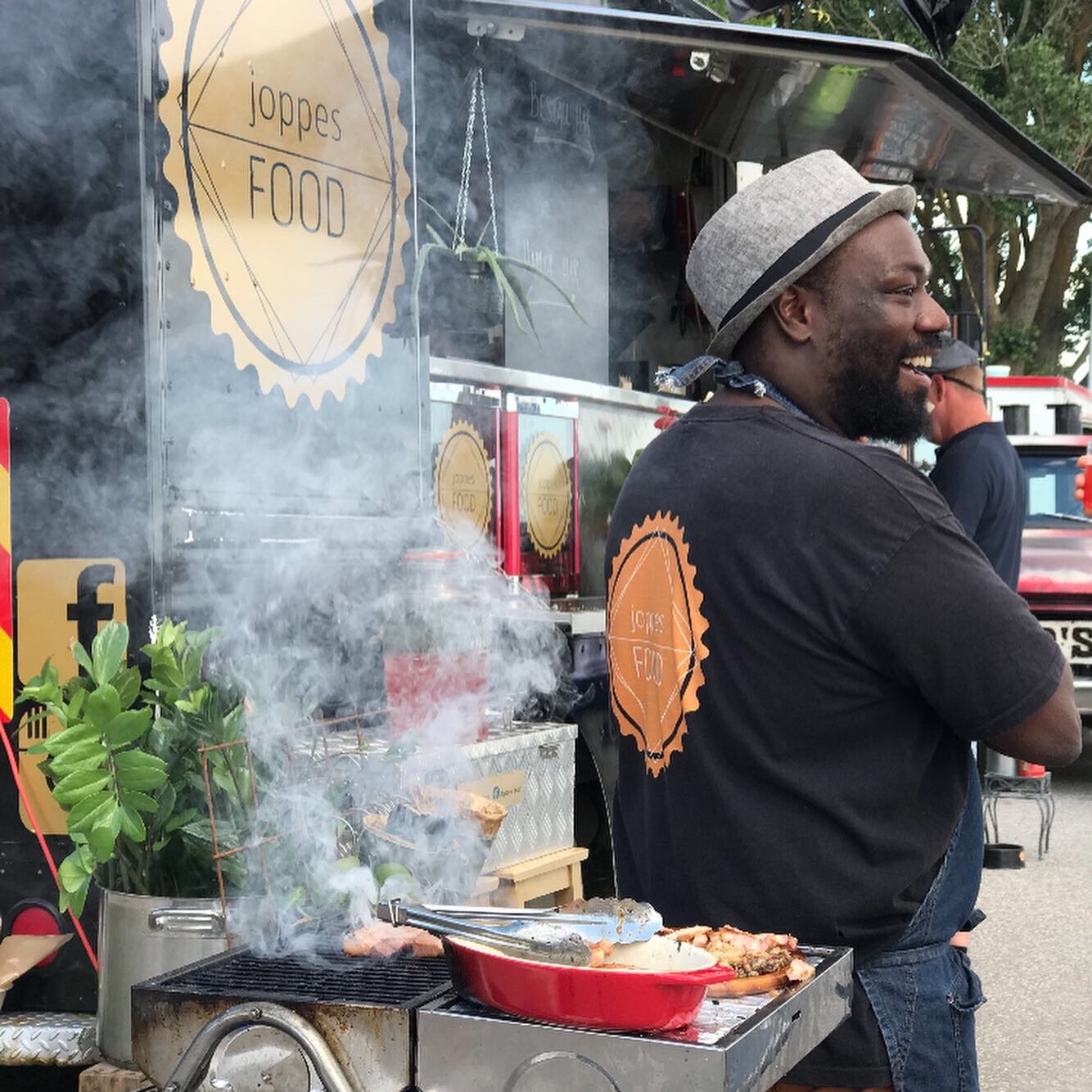 Joppe skrattar vid den rykande grillen framför sin food truck med Joppes Food-loggan